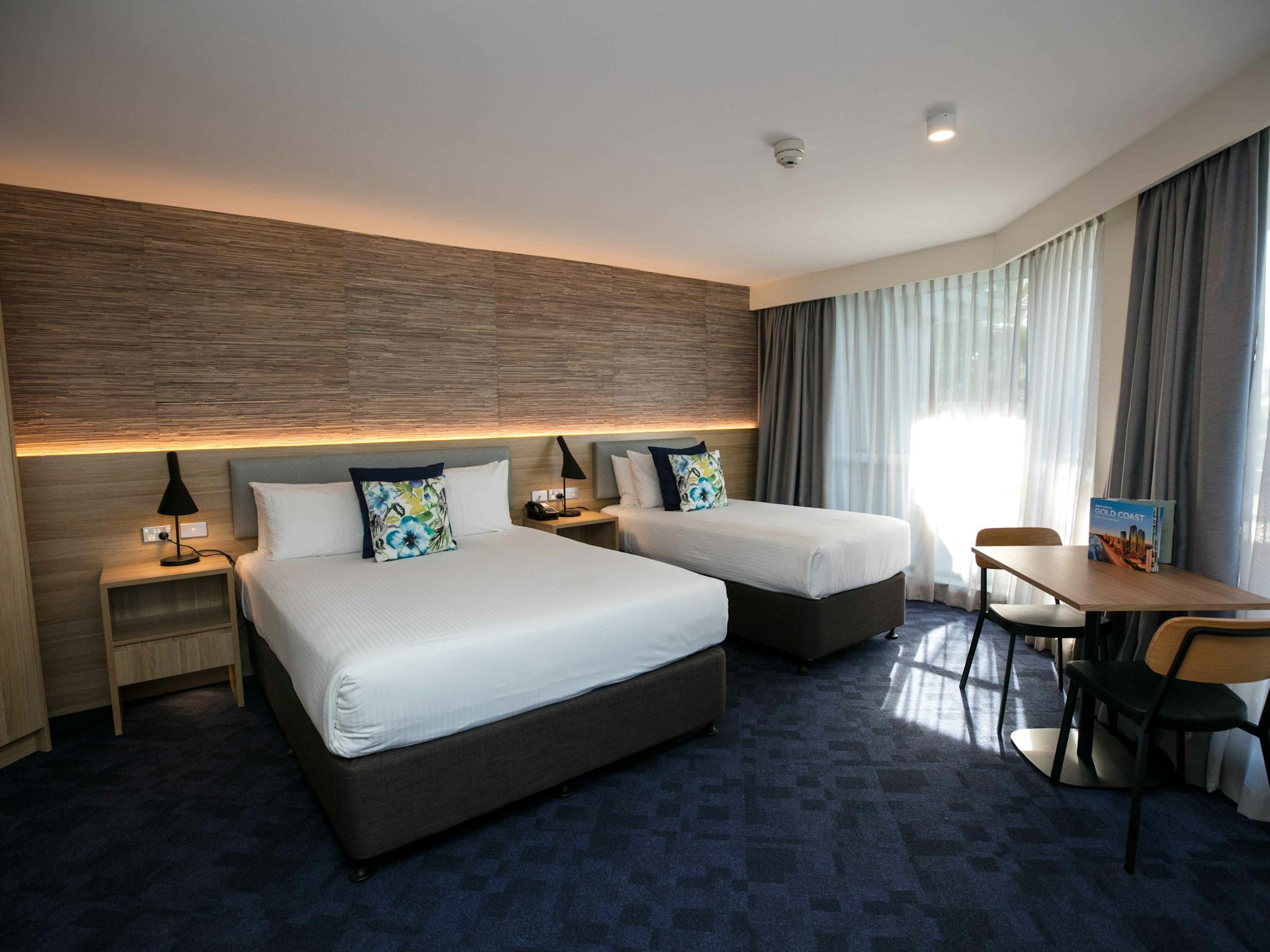 A room with dark carpet and two queen beds and a balcony glass doors covered with a sheer curtain A room with dark carpet and two queen beds and a balcony glass doors covered with a sheer curtain