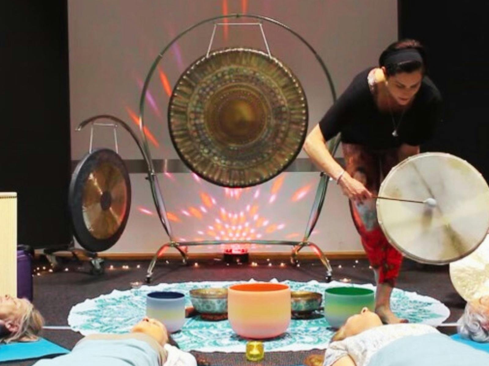 Natalie playing a drum over someone with singing bowls and gongs in background.