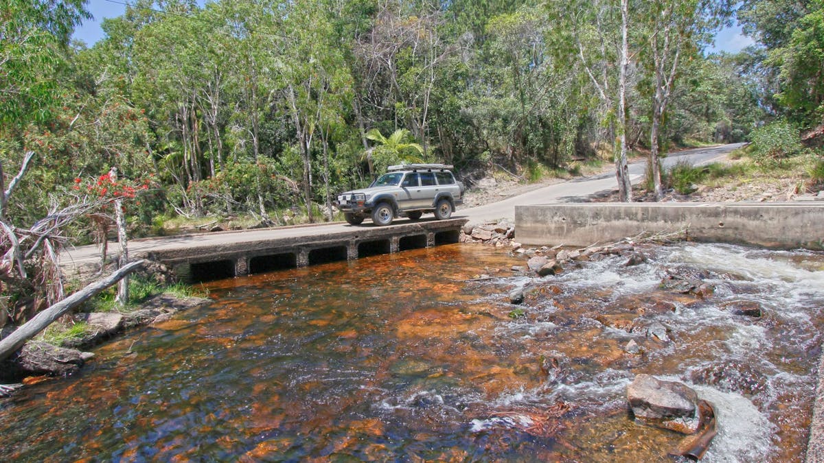 four-wheel drive vehicle driving across bridge over flowing creek