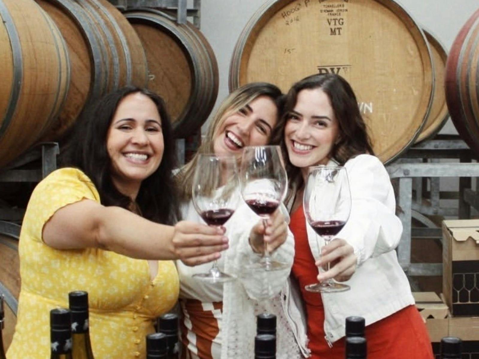 three young woman standing in front of oak barrels raising glasses of red wine