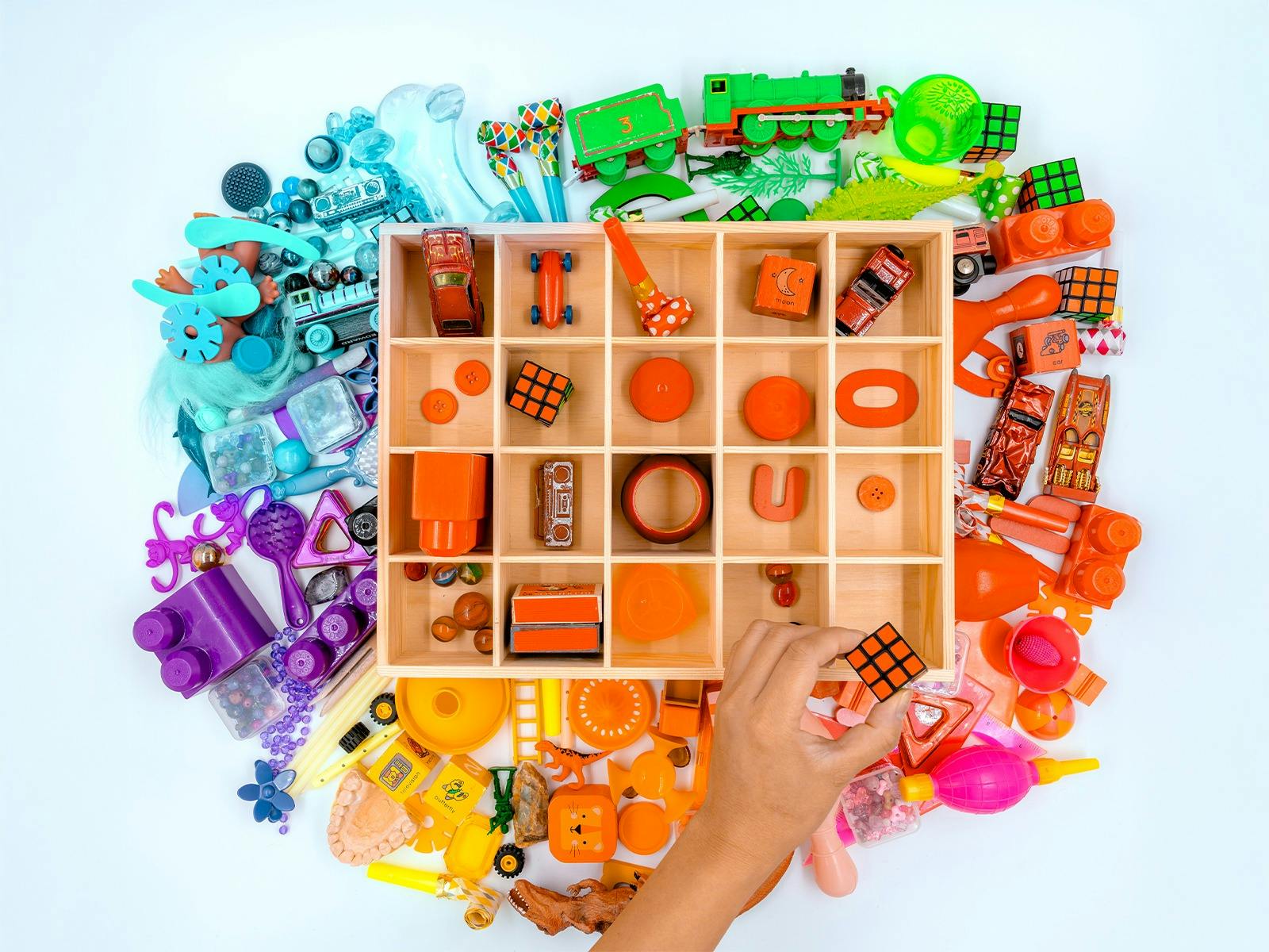 Pile of colourful toys and objects with a wooden shelf on top, also filled with only red objects.