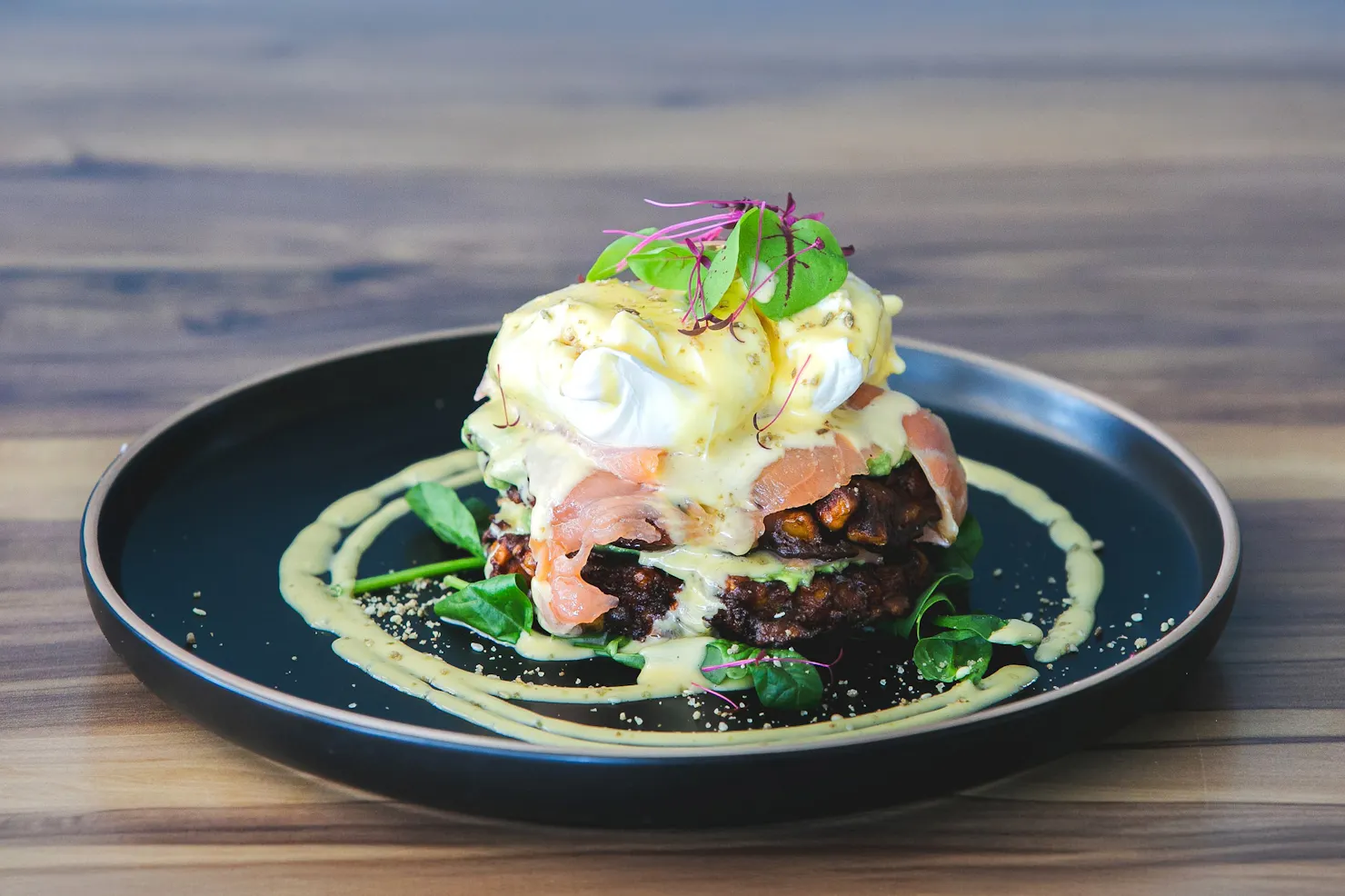 Corn fritters with poached eggs, avocado and fresh greens on a dark plate