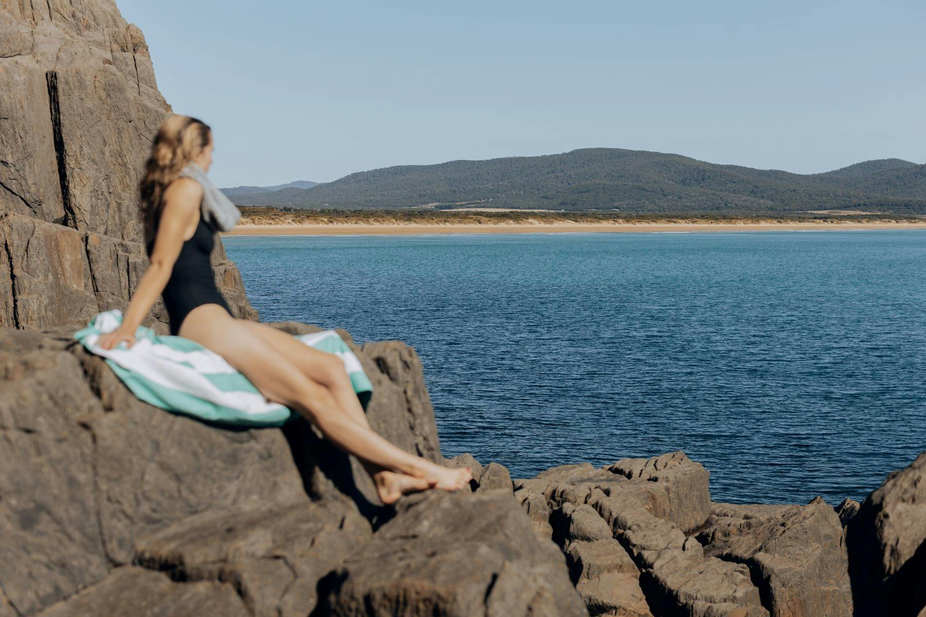 Woman sitting on rocks at edge of ocean