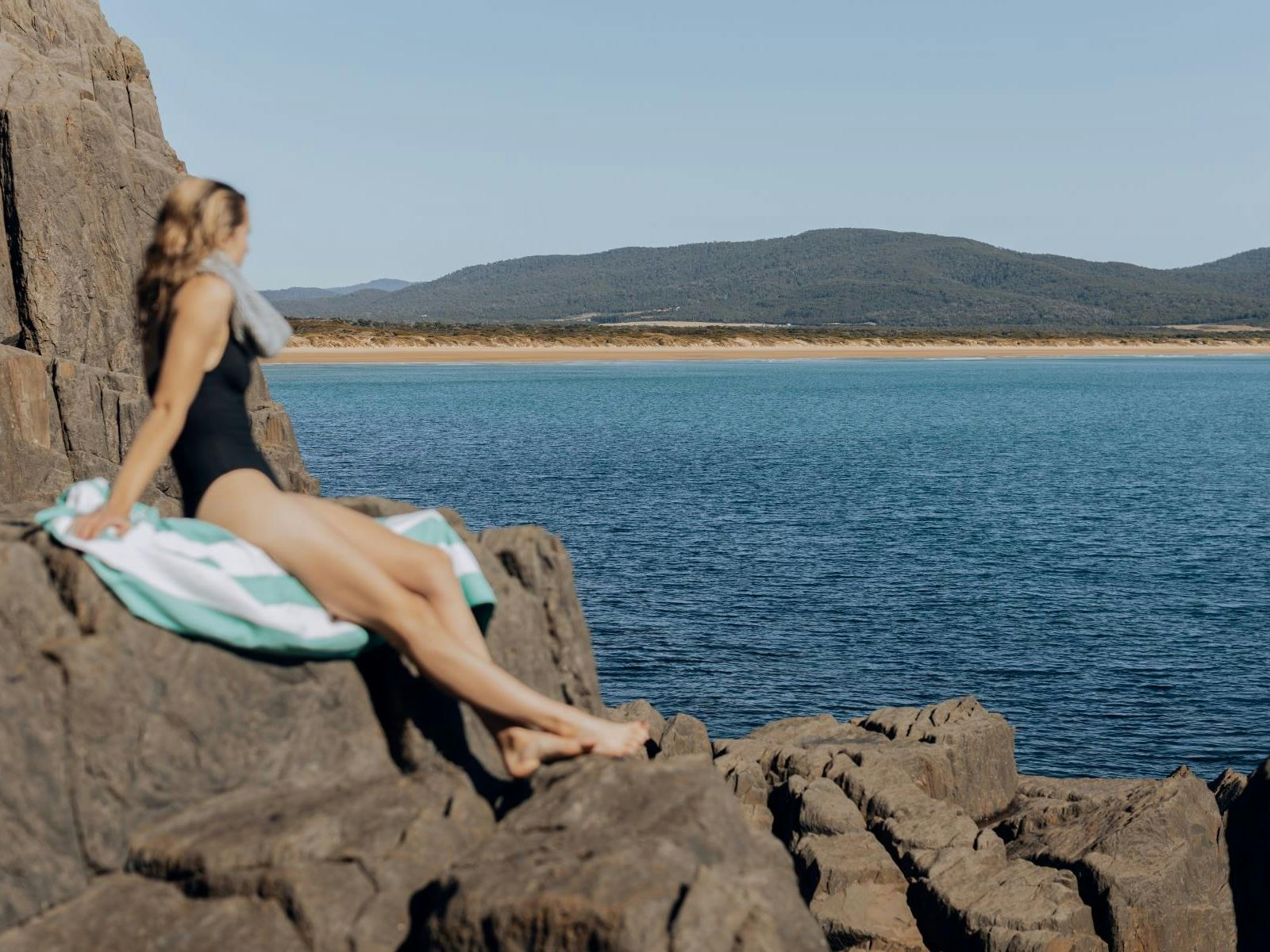 Woman sitting on rocks at edge of ocean