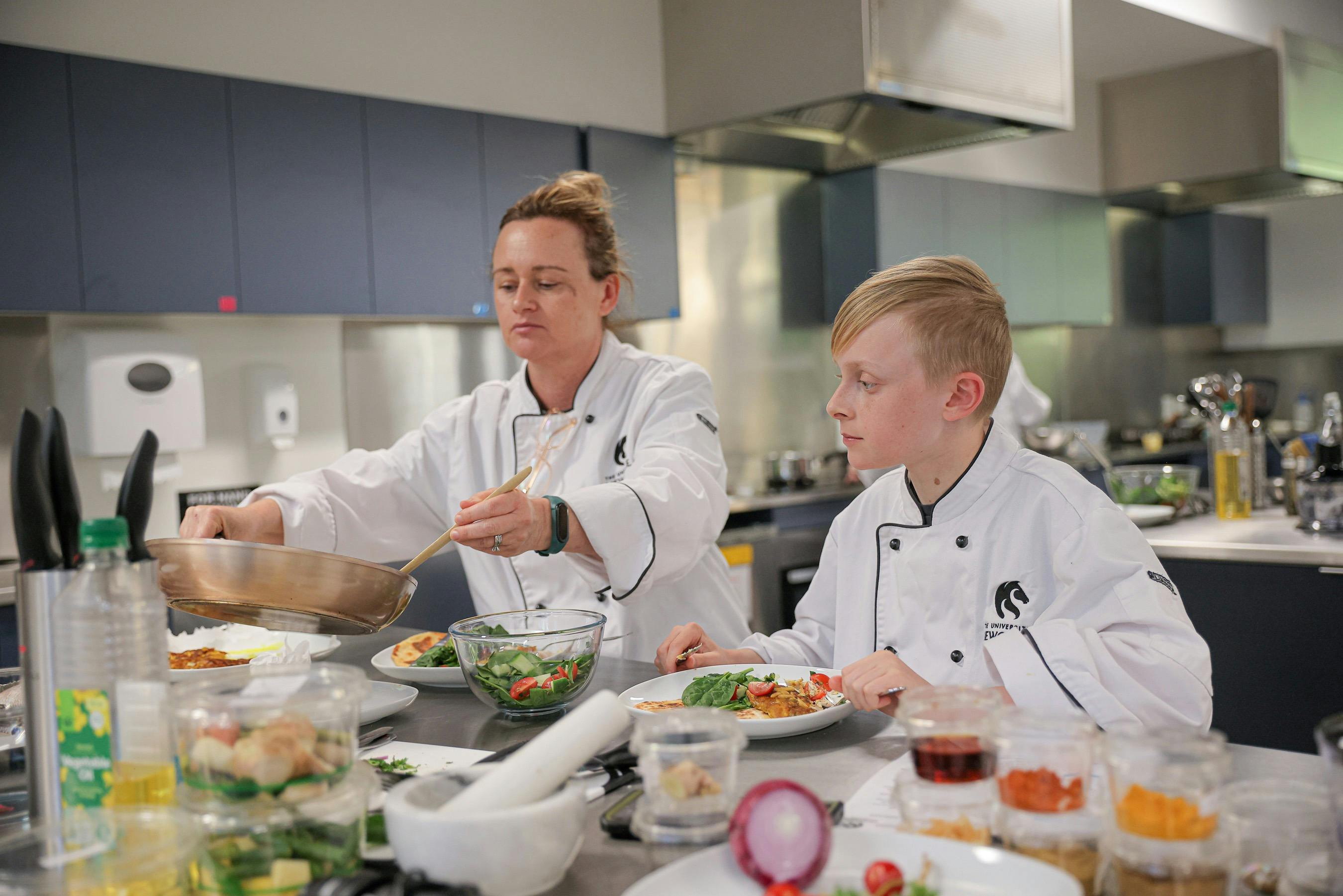 A woman and boy in white chef uniforms cooking seafood.
