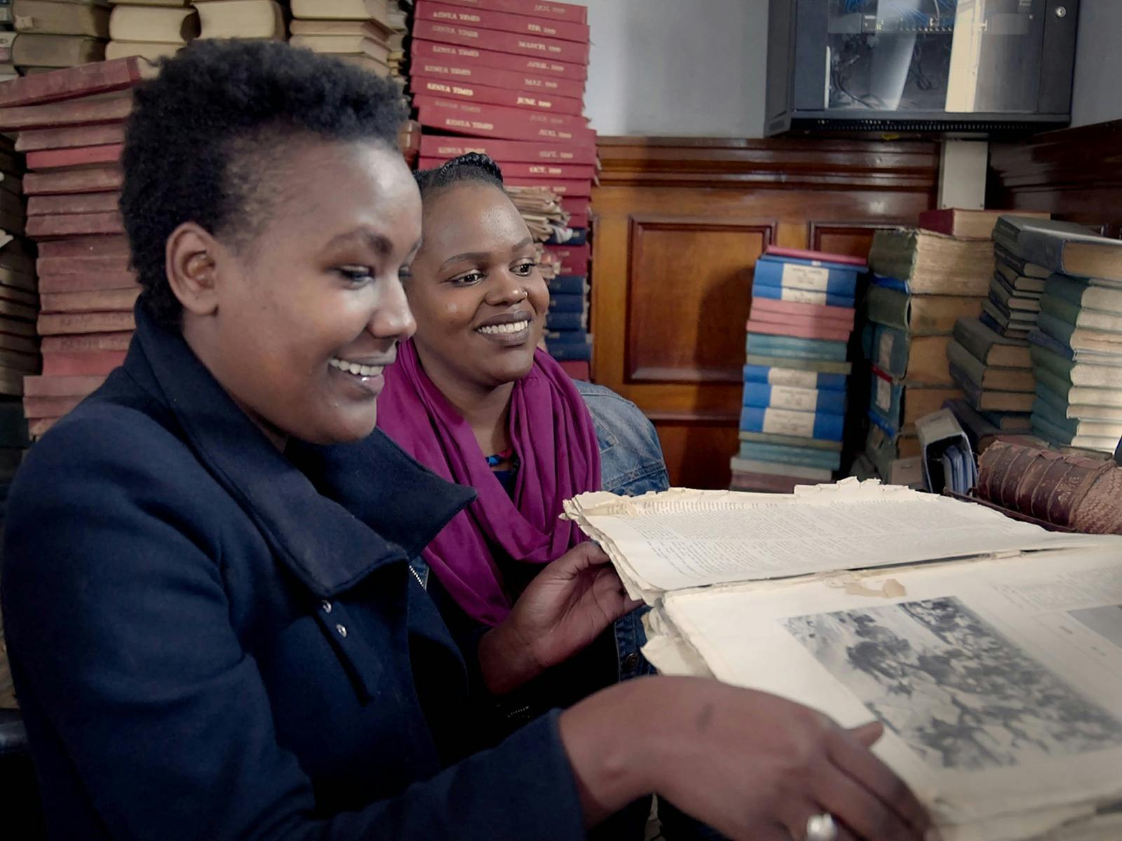 Two women reading books in a room full of books and manuscripts