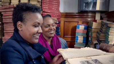 Two women reading books in a room full of books and manuscripts