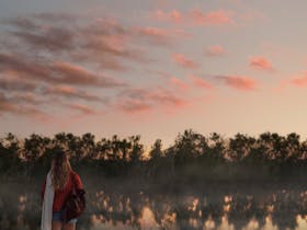 A woman stands at the edge of the springs, a towel slung over her shoulder.