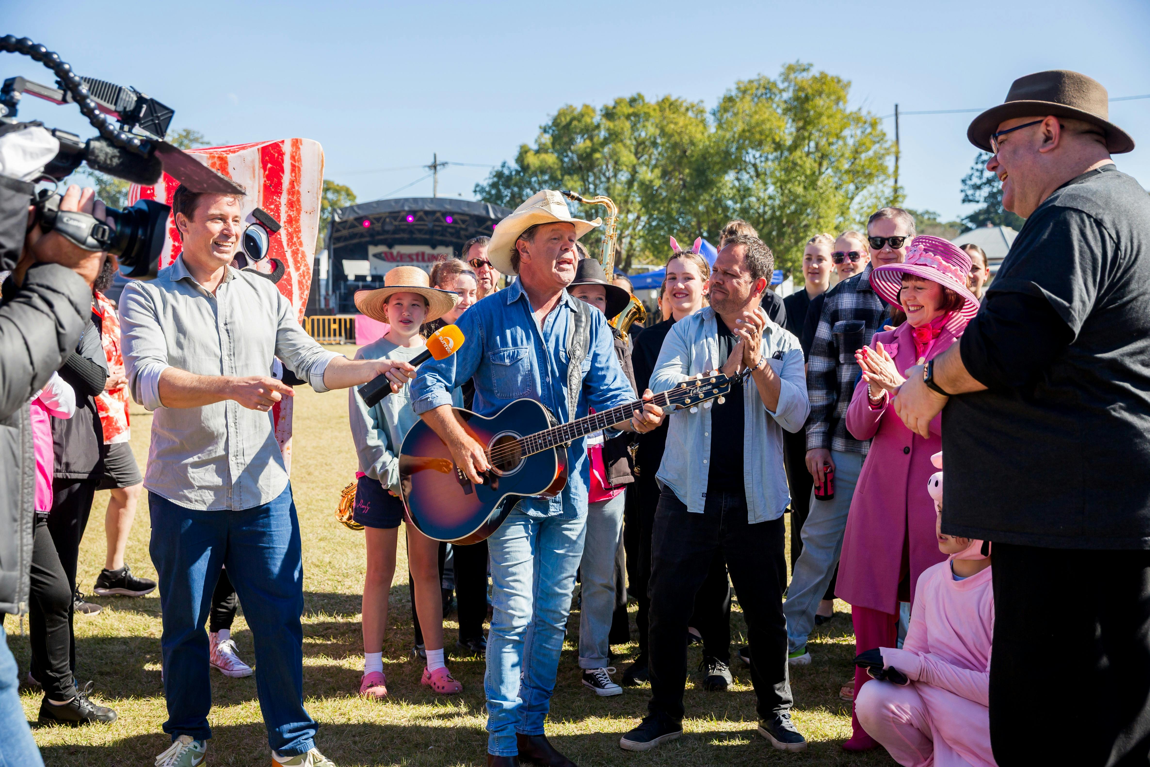 James Tobin is holding a microphone out towards Troy Cassar-Daley who is playing his guitar.