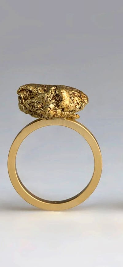 Three rings with raw lumps of metal stand upright; one silver, one gold and one copper