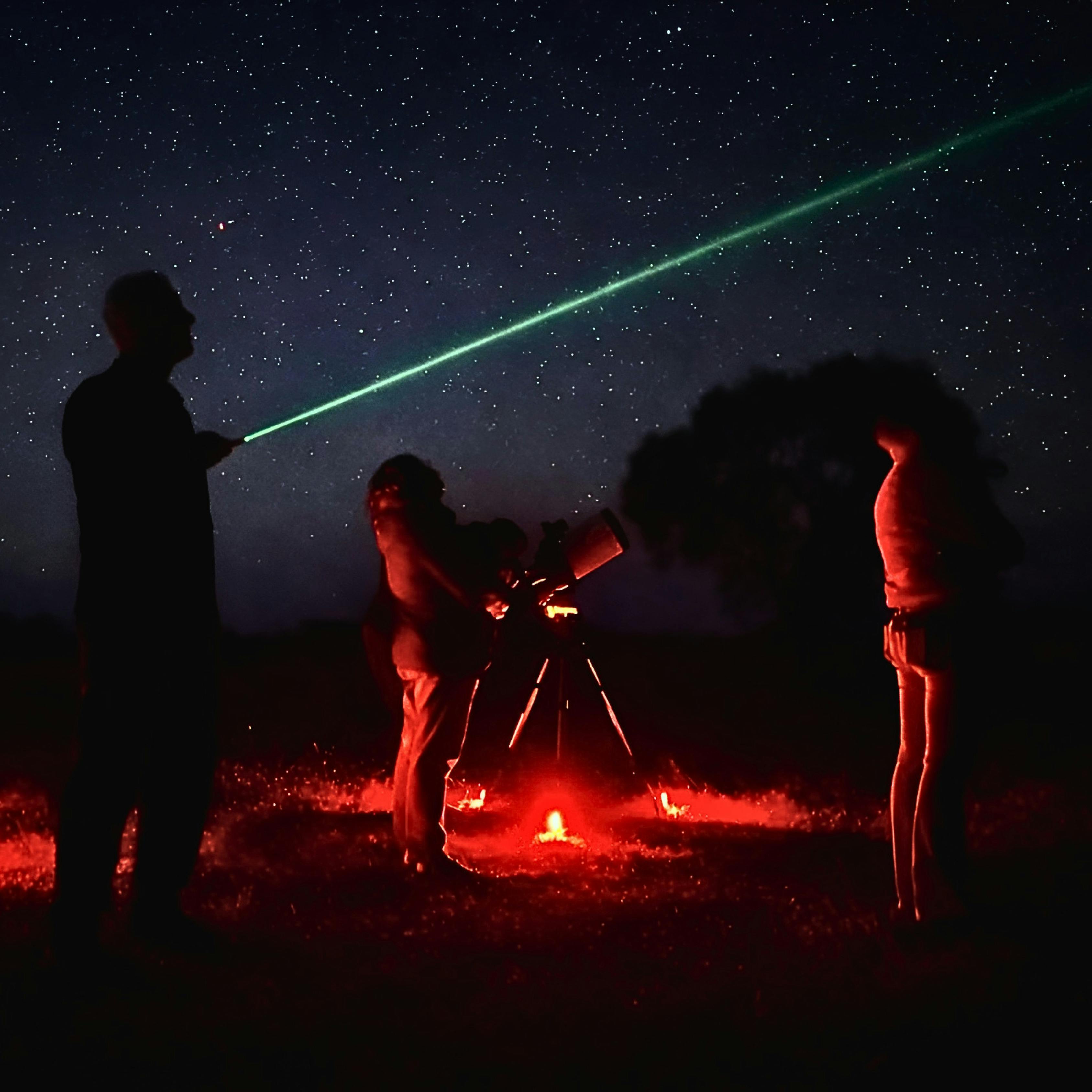Astronomy guide using a green laser to point out stars as guests observe through a telescope