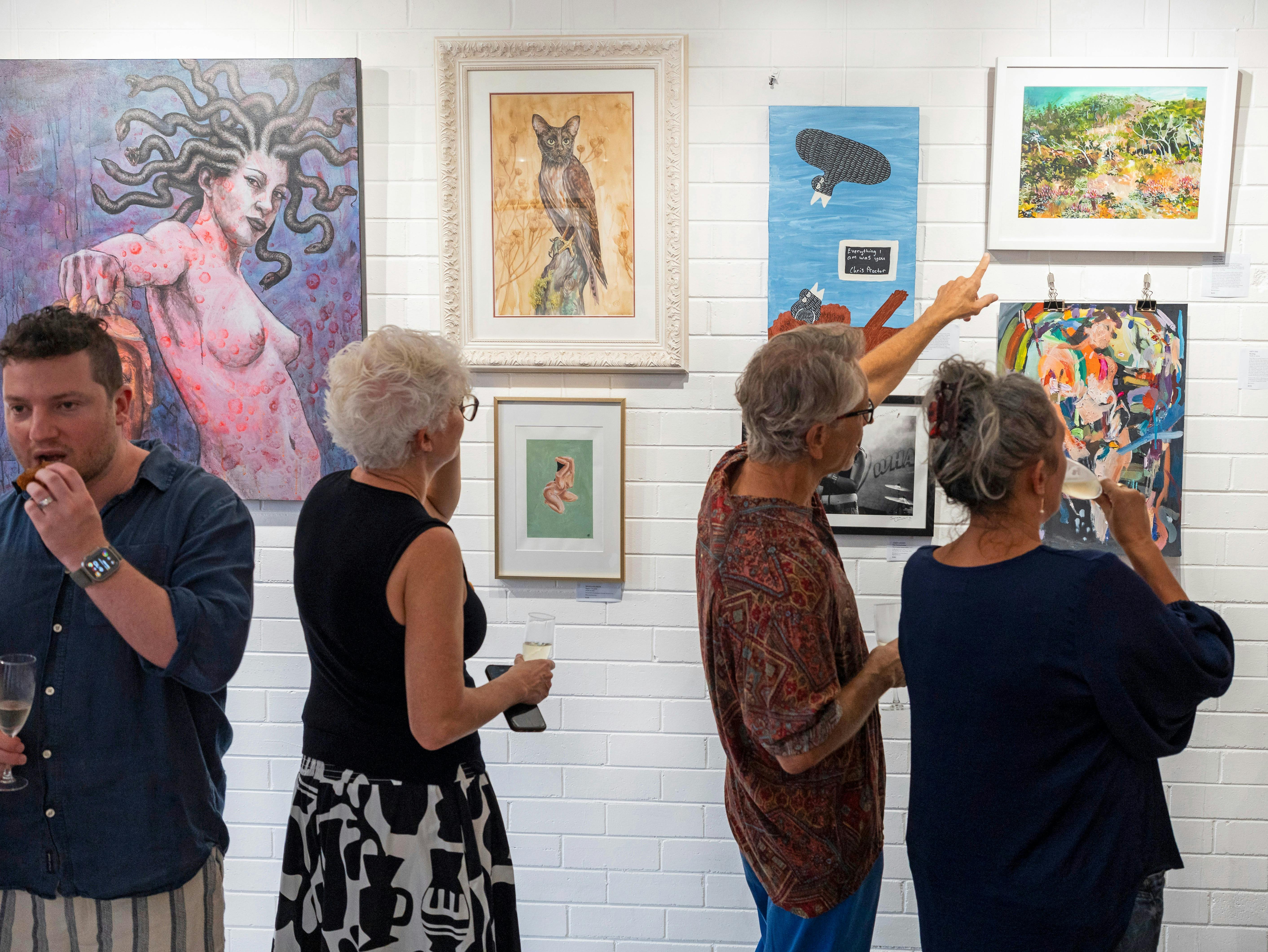 Guests look and point at work on the walls of The Laneway Gallery opening exhibition.