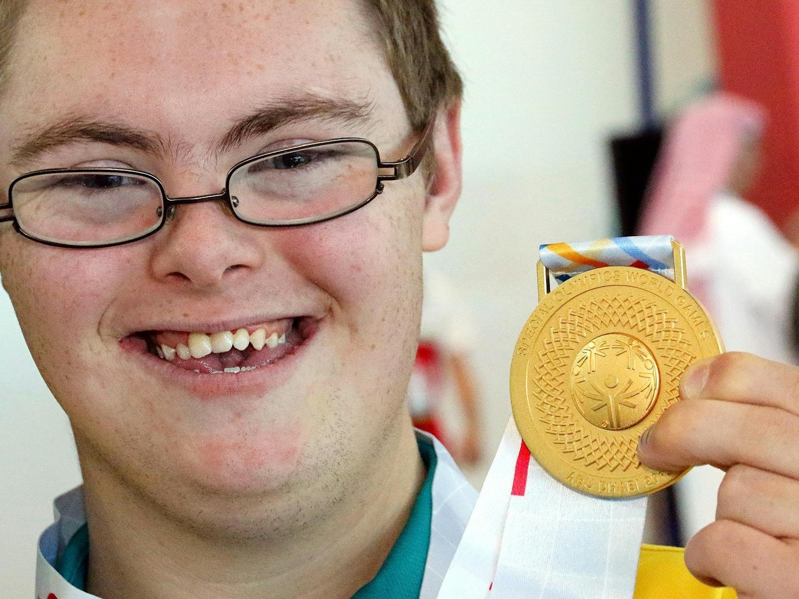 person smiling holding gold medal.