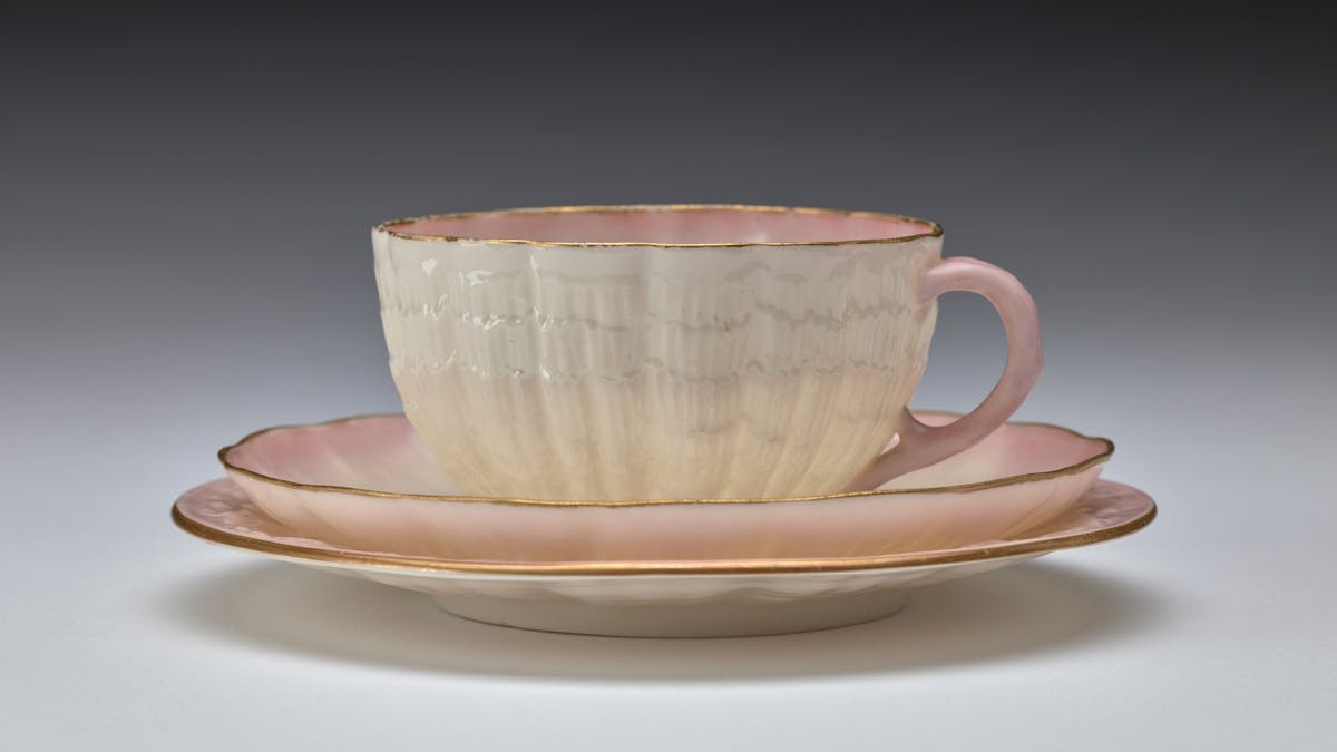 A delicate pink and cream tea cup rests on a saucer and plate