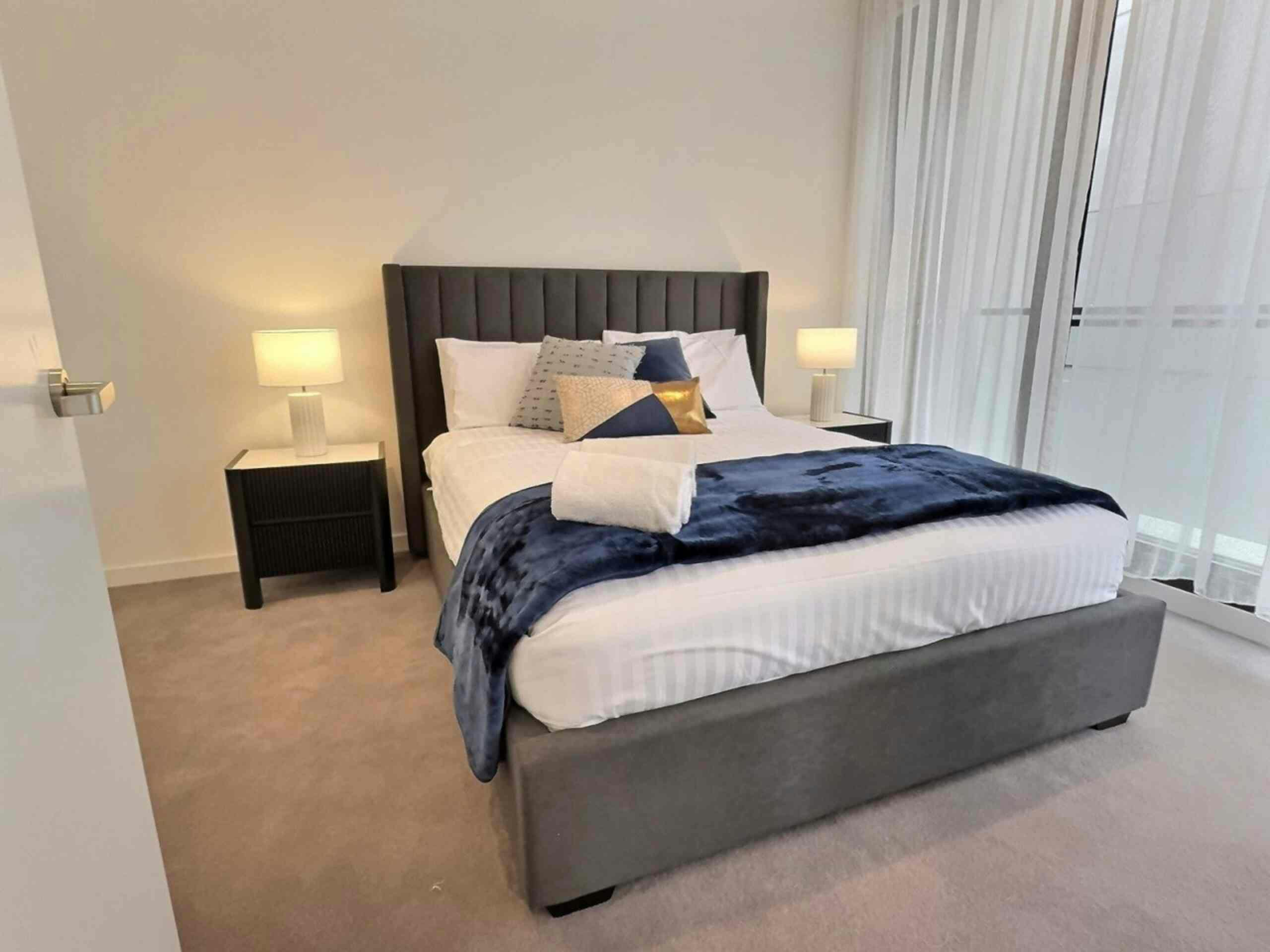 Modern bedroom with a grey tufted bed, navy throw blanket, bedside tables, and lamps.