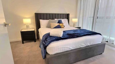 Modern bedroom with a grey tufted bed, navy throw blanket, bedside tables, and lamps.