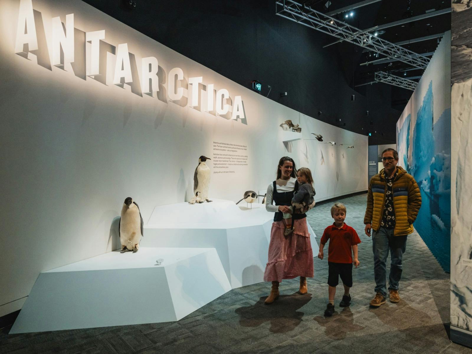 Young family walking together in front of a penguin display.