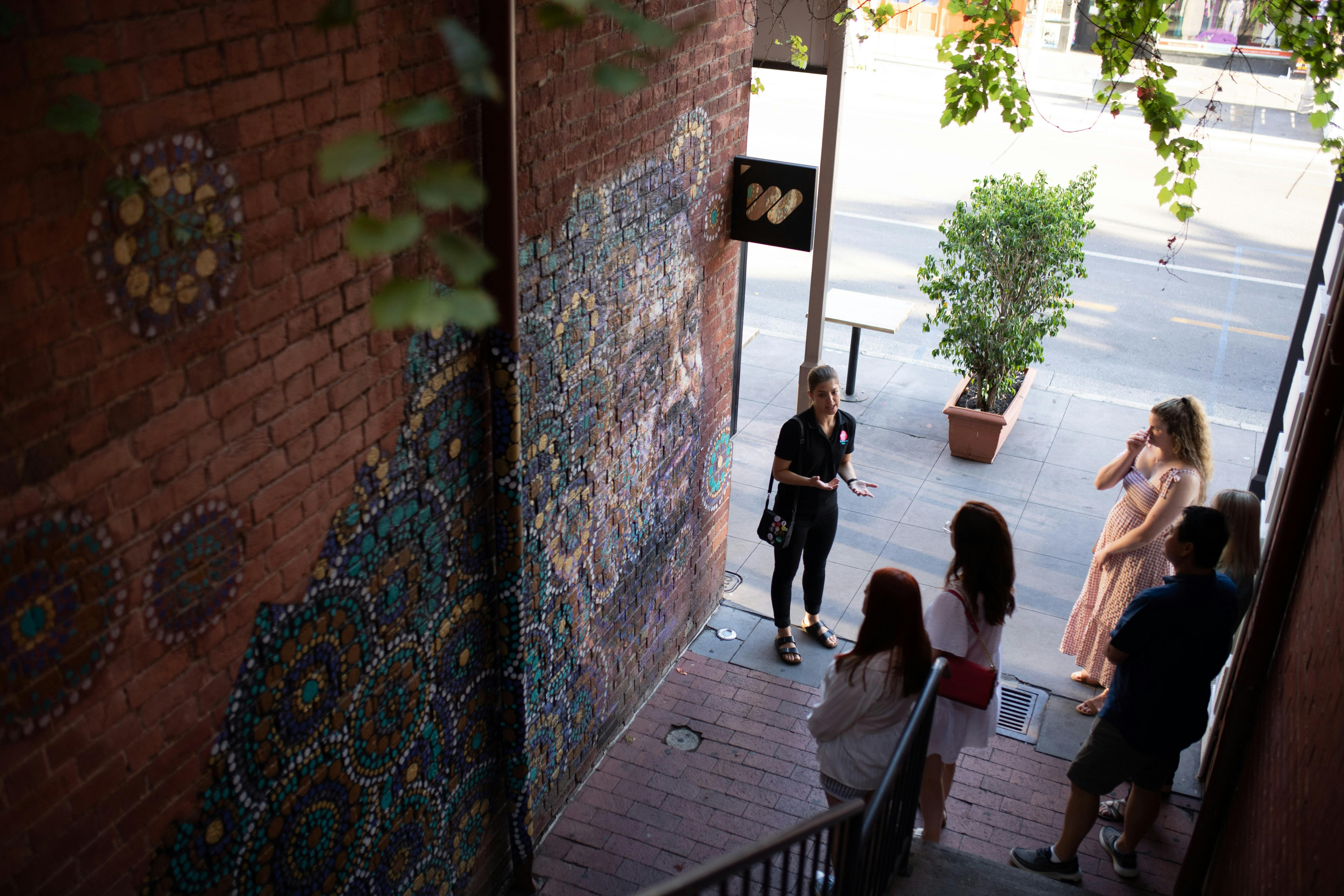 A view from above shows guests on tour admiring an artwork of an Indigenous role model in Adelaide.