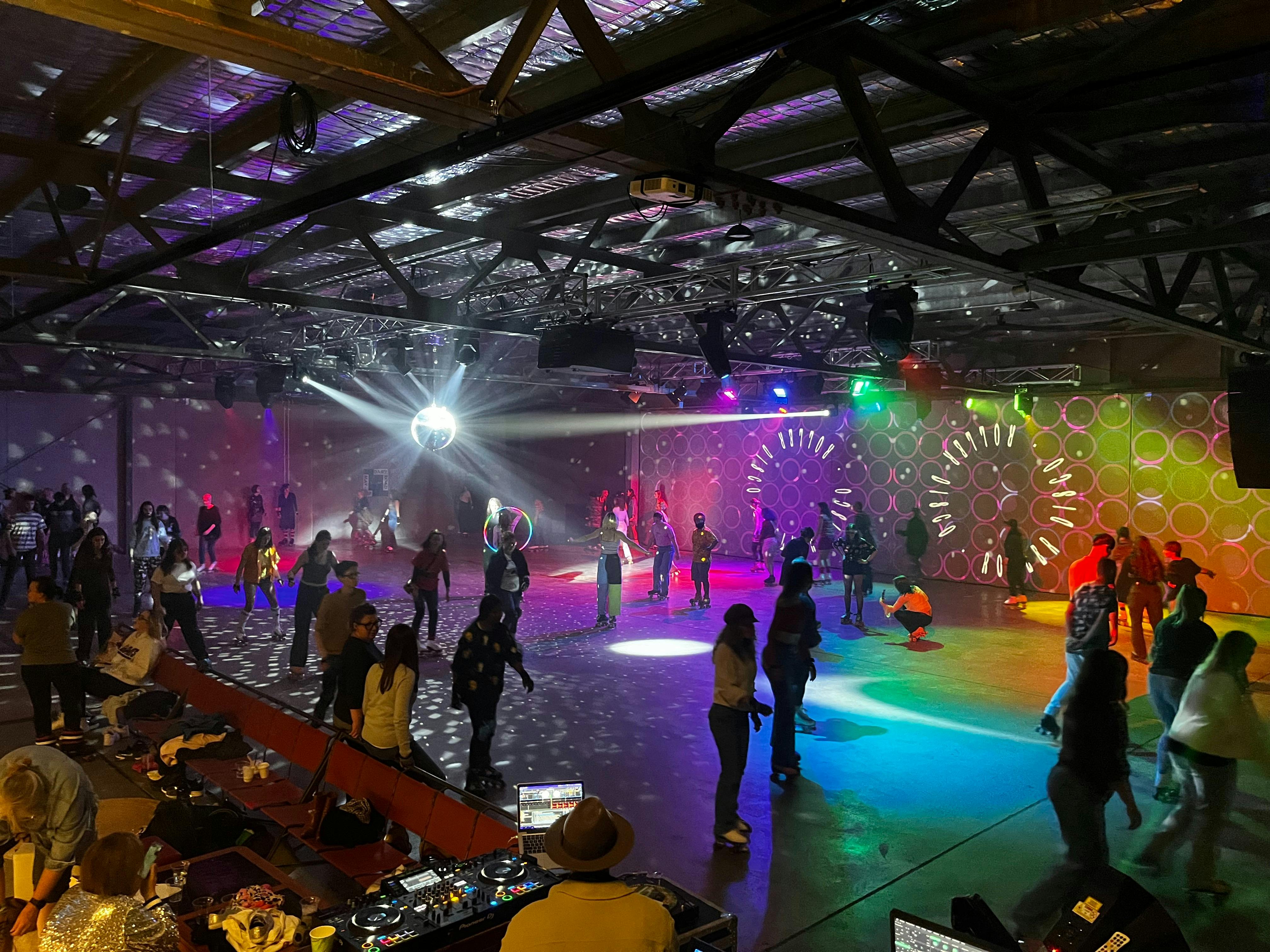 Large indoor space with shining lights and lots of people roller skating