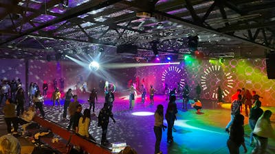 Large indoor space with shining lights and lots of people roller skating