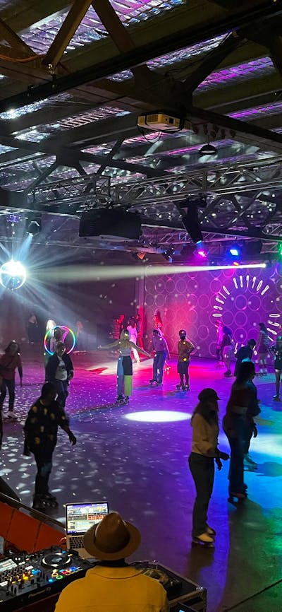 Large indoor space with shining lights and lots of people roller skating