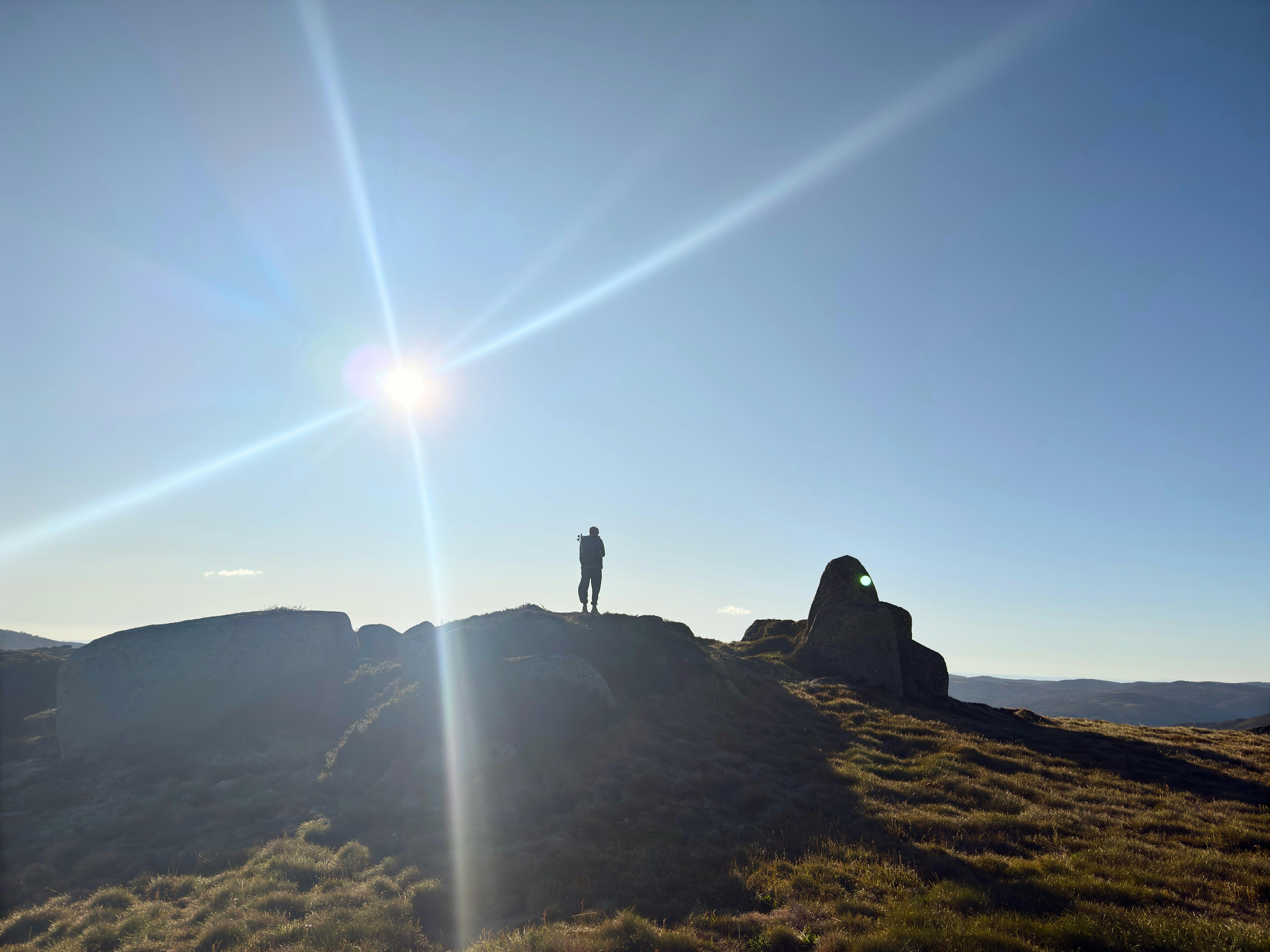 A hiker standing on a rock with the sun behind.