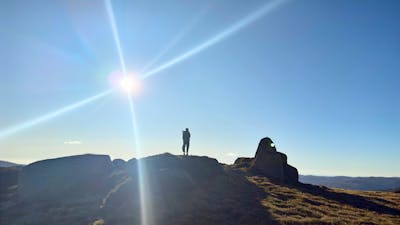 A hiker standing on a rock with the sun behind.