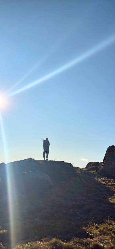 A hiker standing on a rock with the sun behind.