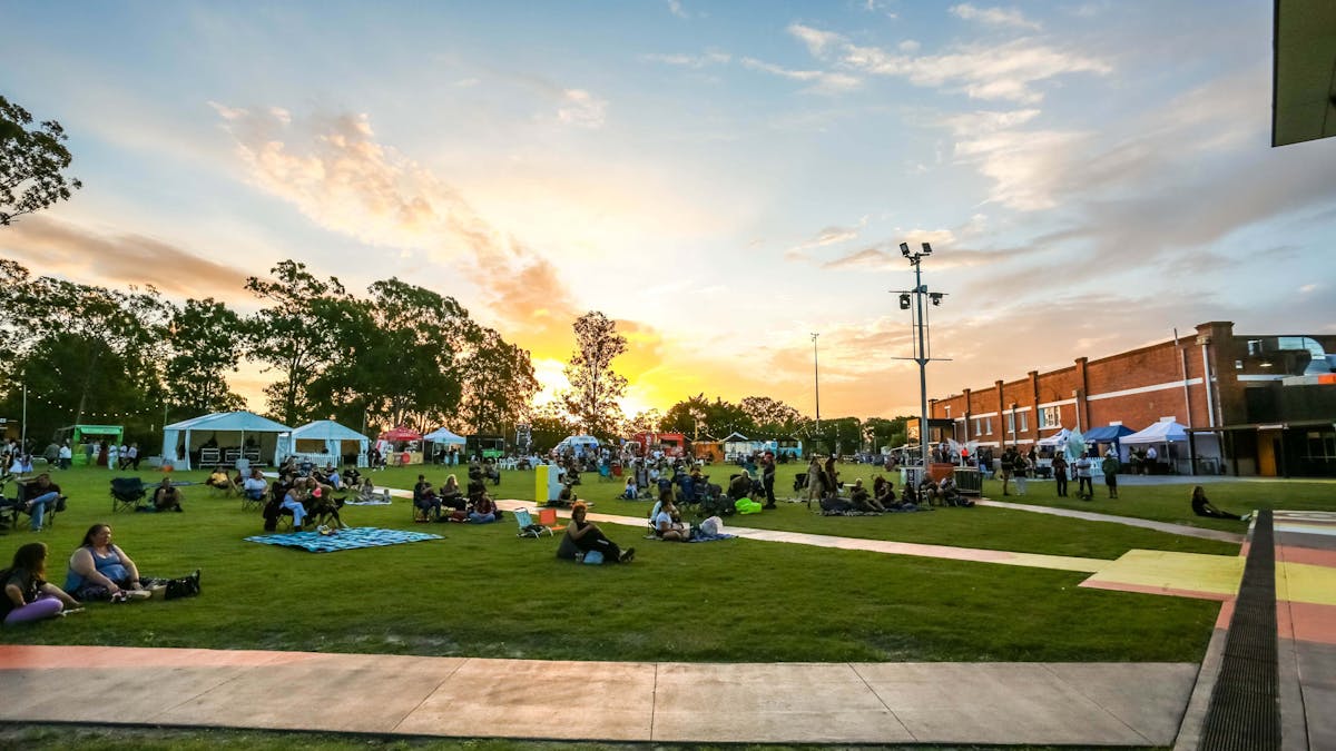 People sitting on grass with butter factory building in the background.