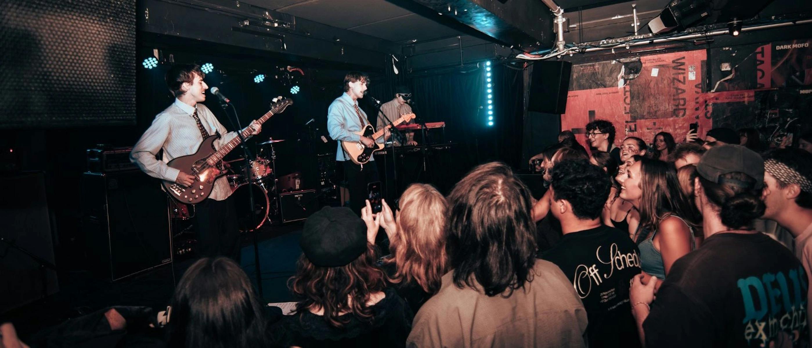 Two men on stage playing guitar and singing in front of an audience of young people