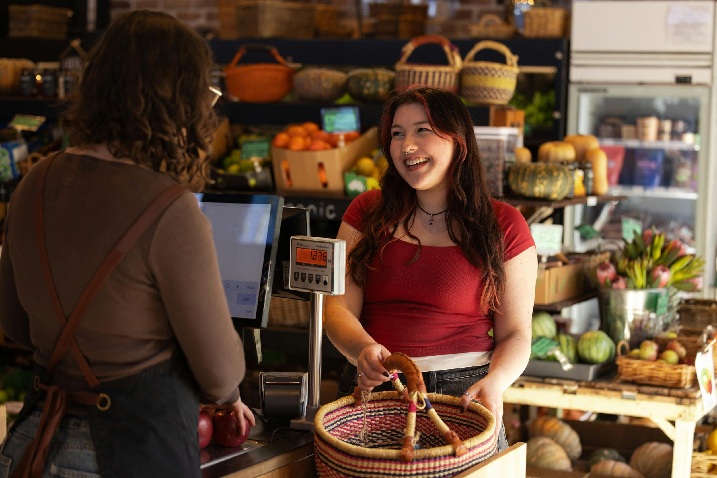 Smiling woman served at the check-out, using woven basket, colour fruit in the background