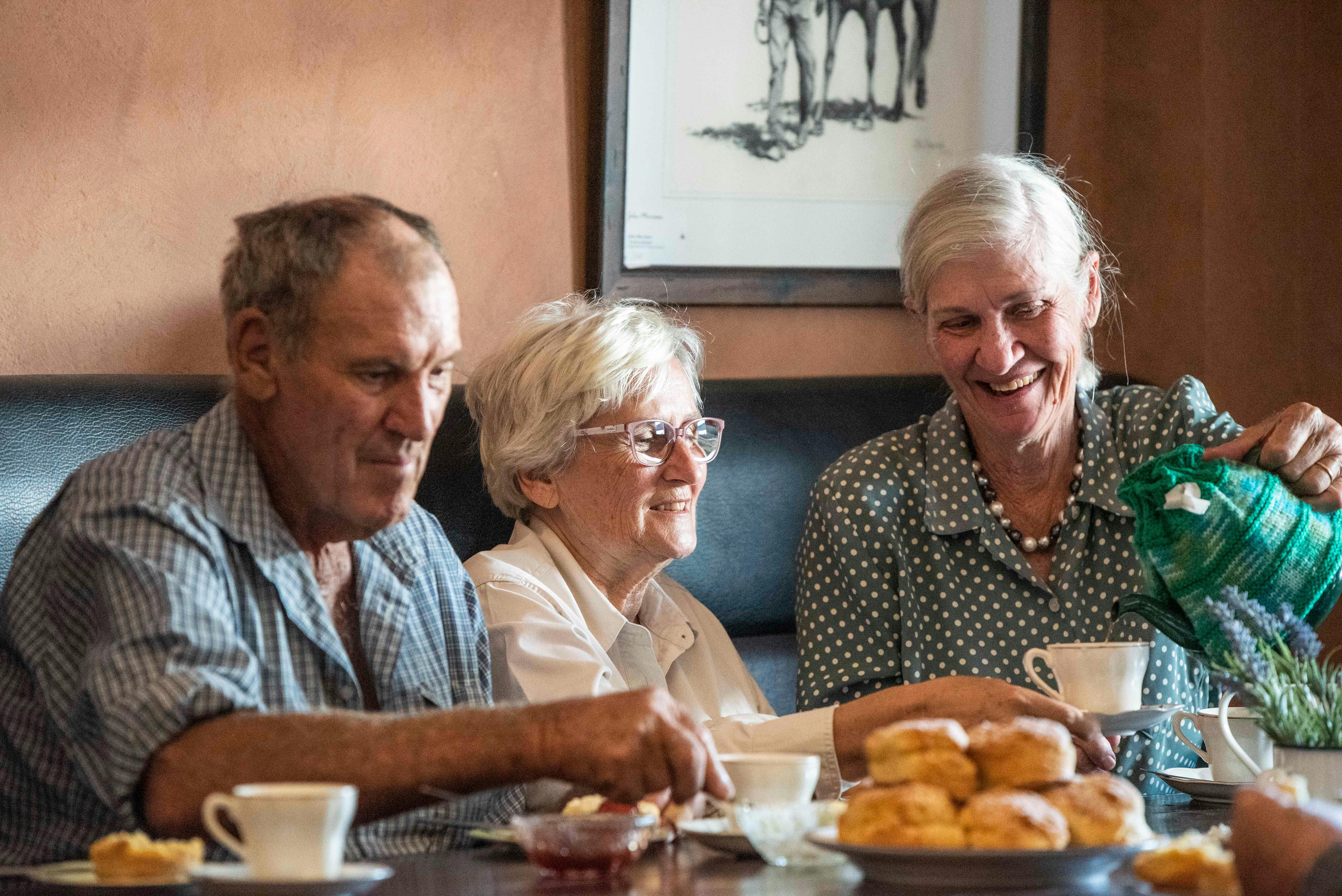 People sitting at a table with scones, jam and cream. A lady is pouring tea