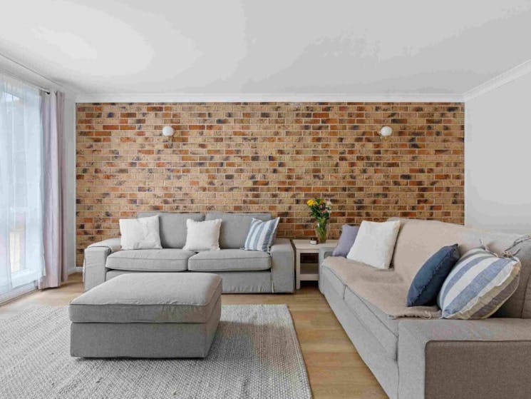 Loungeroom with spacious fabric lounges, coastal styling and feature brick wall