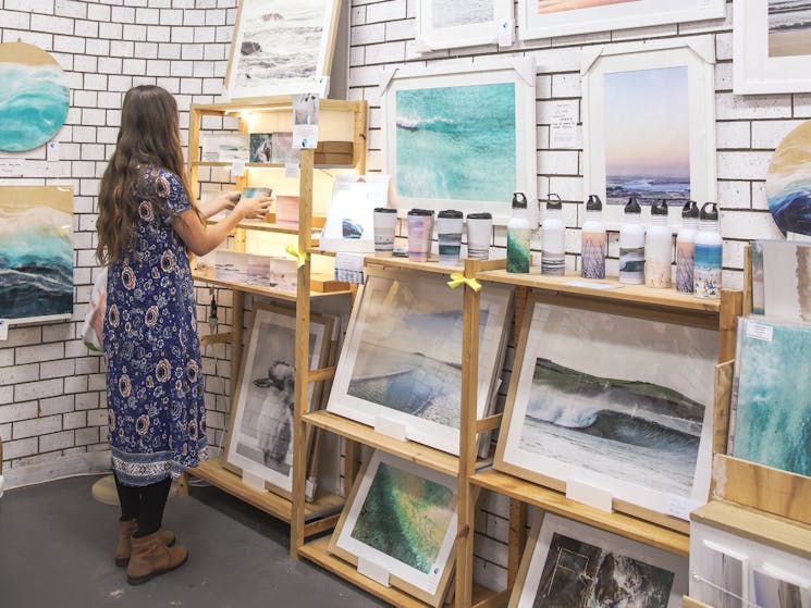woman in purple floral dress looking at art and homewares with a coastal subject matter