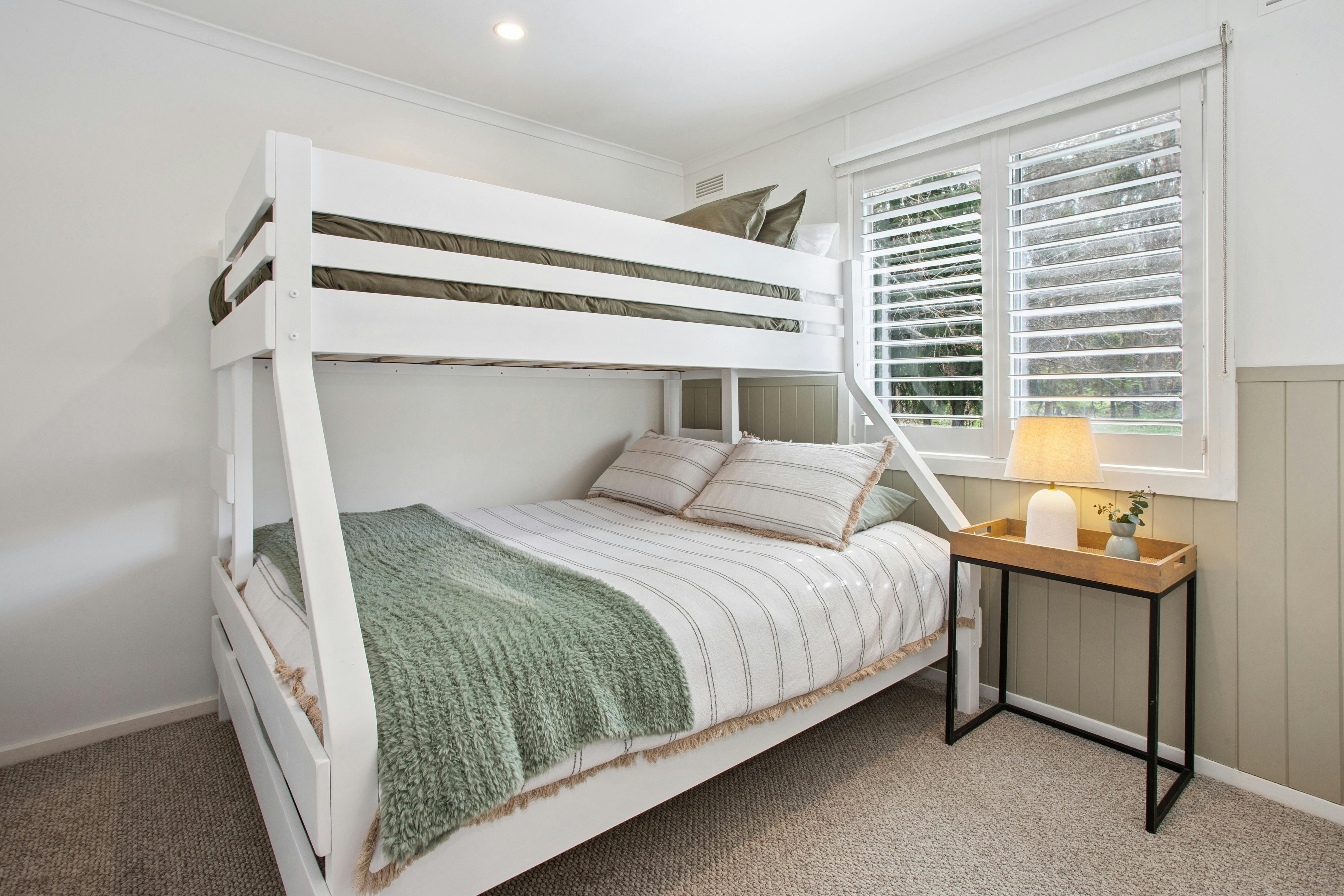 Bedroom with white bunk bed, striped linen, bedside lamp and plantation shutters
