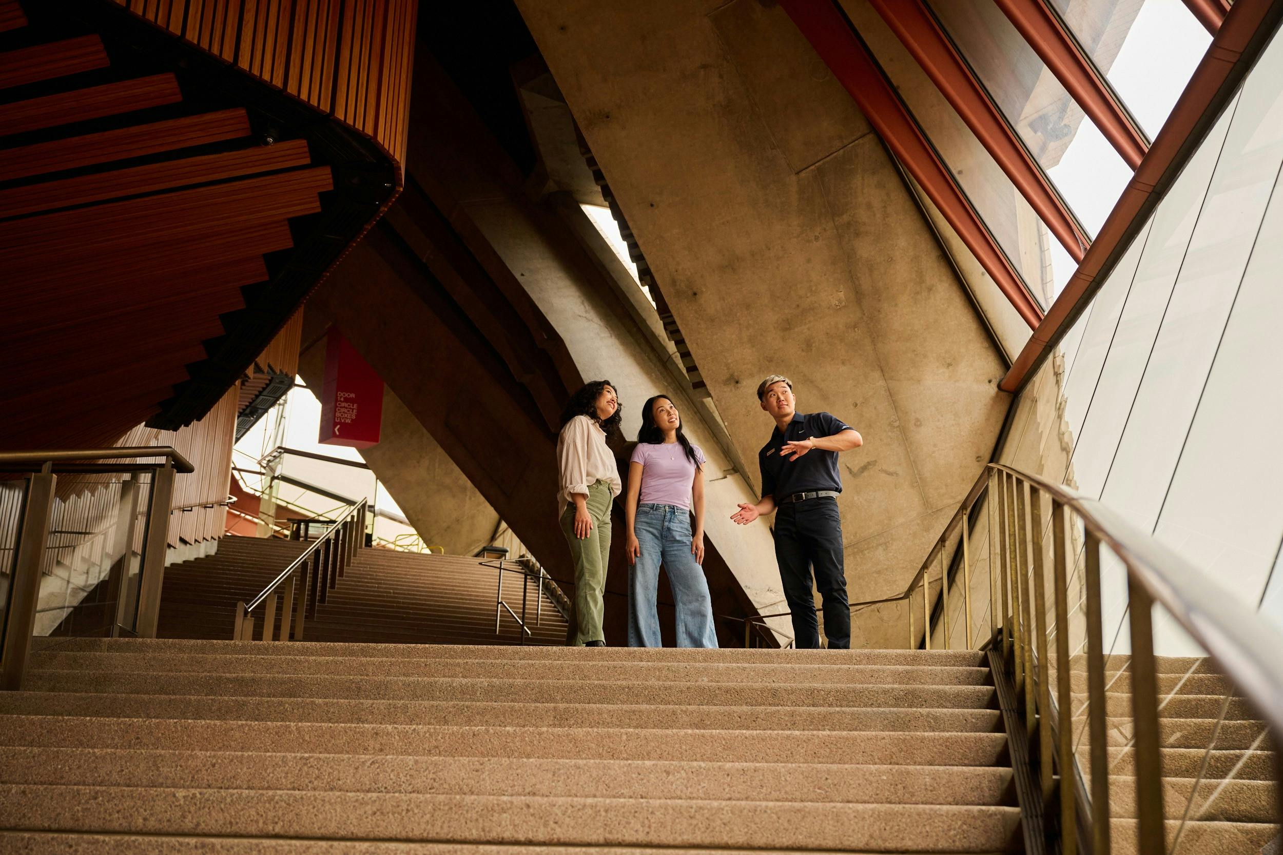 Tour guide and two women standing at the top of the stairs looking out the window