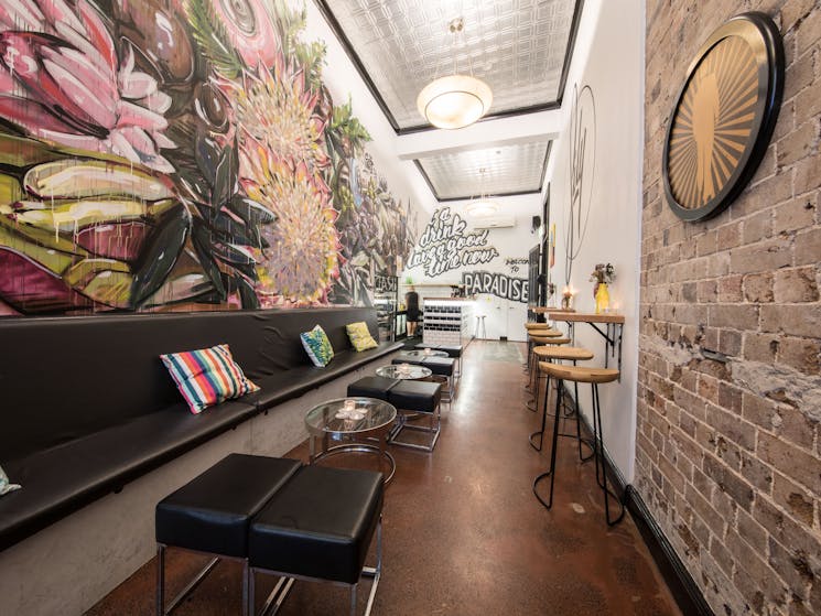 A narrow indoor seating area with banquette down one side, and colorful mural of flowers on the wall