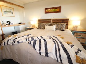 Wide angle photo of king bed in room with bedside tables and refreshment area, in beachside colours.