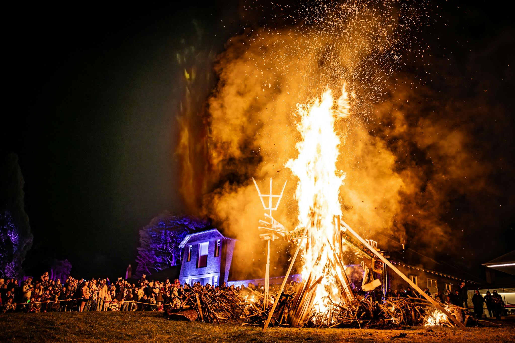 A large burning sculpture in front of an art gallery surrounded by a large crowd