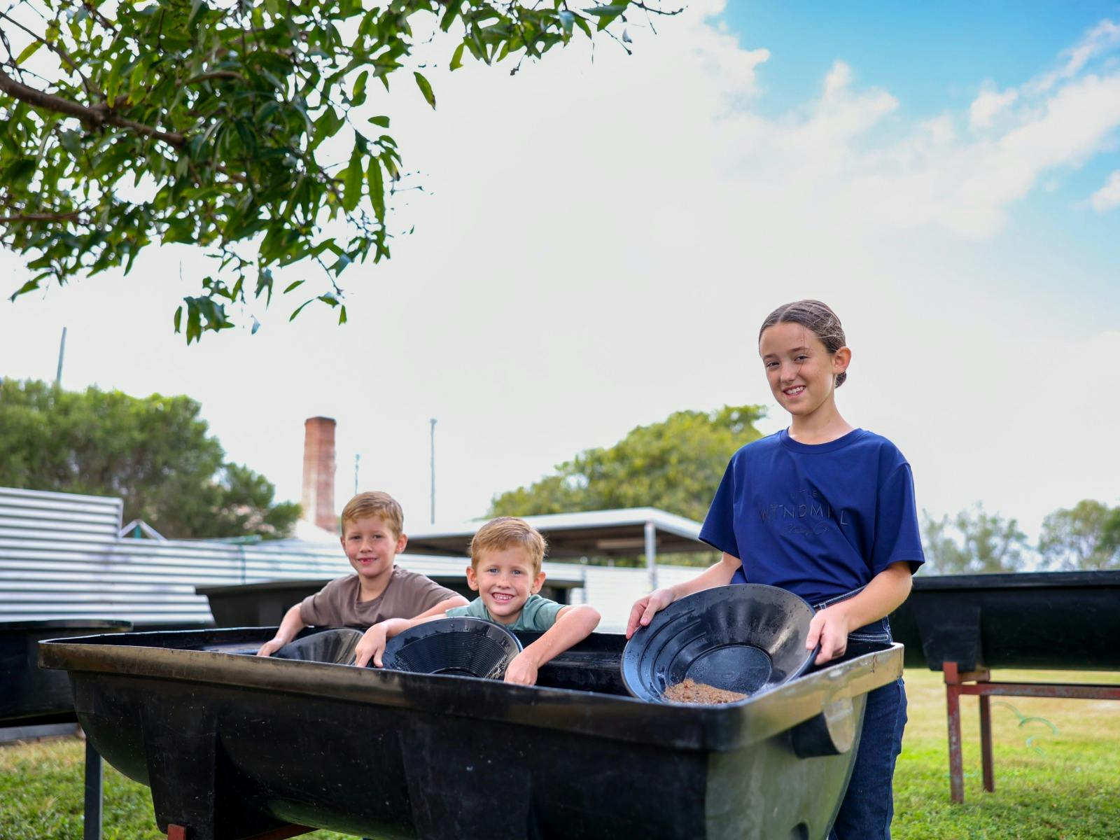 3 kids panning for gold in a trough