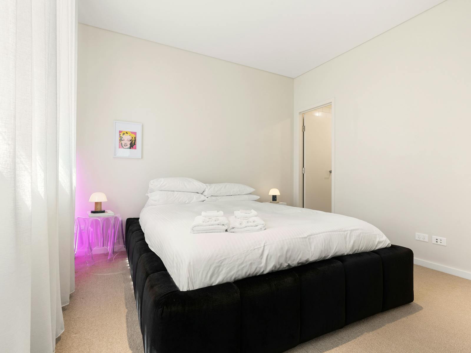 Cozy bedroom with a stylish black velvet bed and bright lighting.
