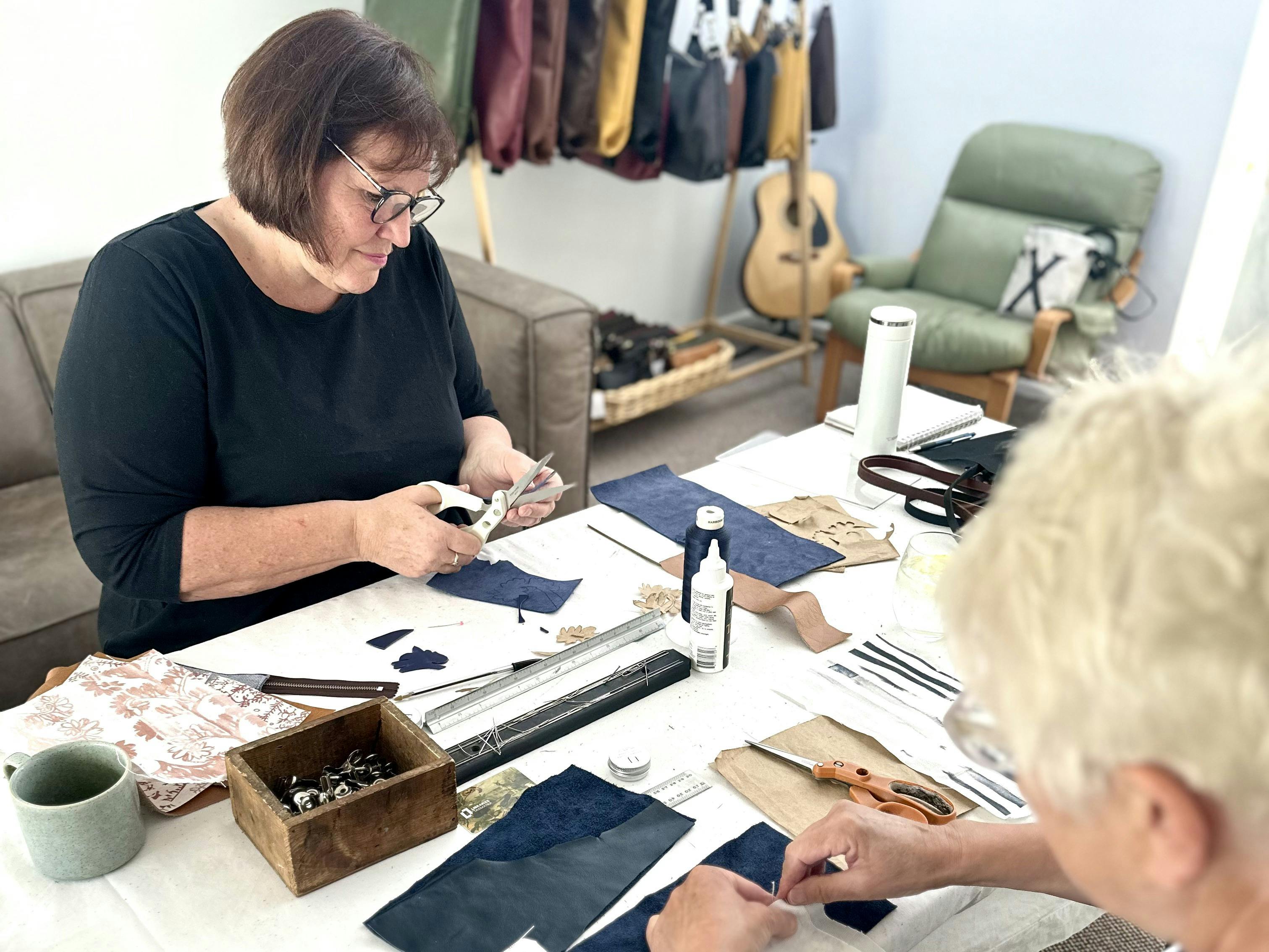 Participants working on leather projects during a workshop, surrounded by crafting materials like fa
