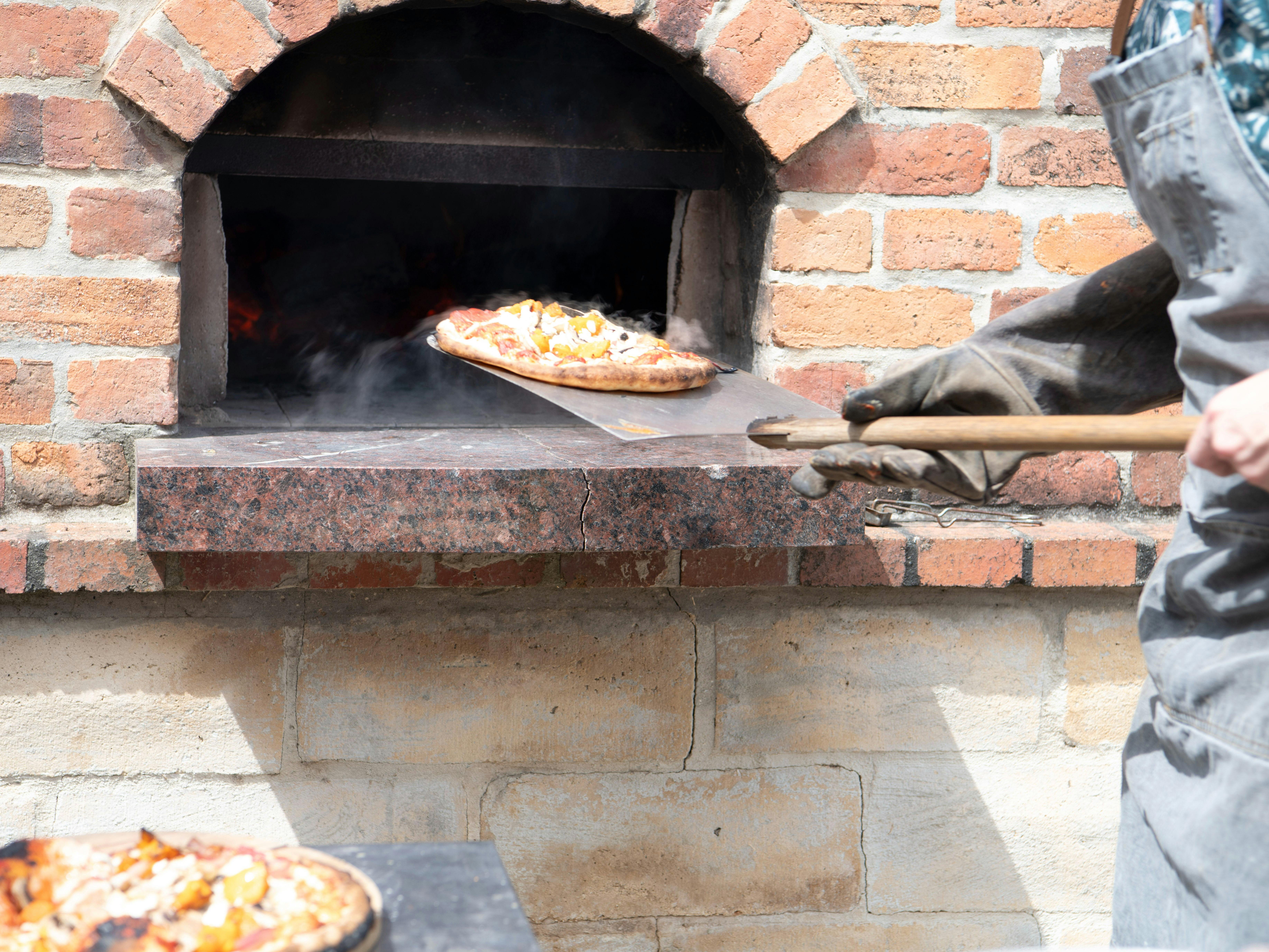 Cooked wood fired pizza emerging from the oven
