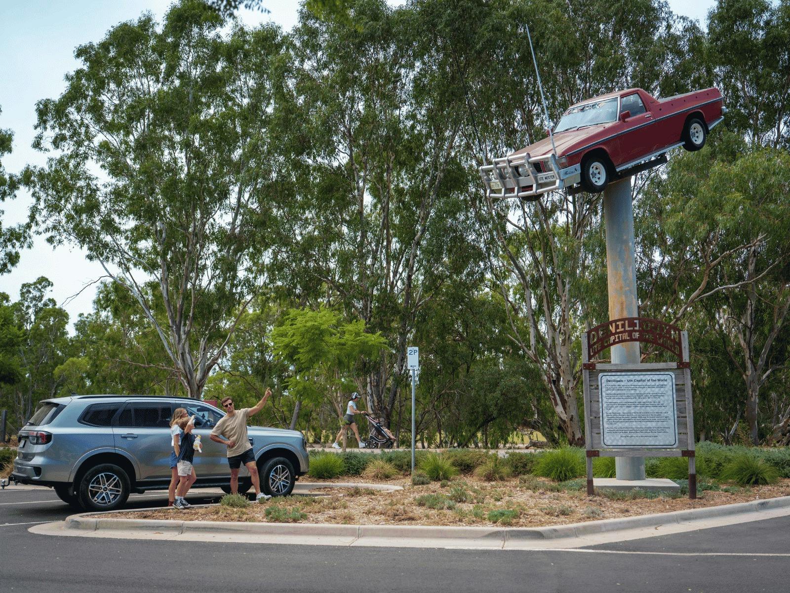 A wide shot of a red ute on a pole next to a car park with gumtrees