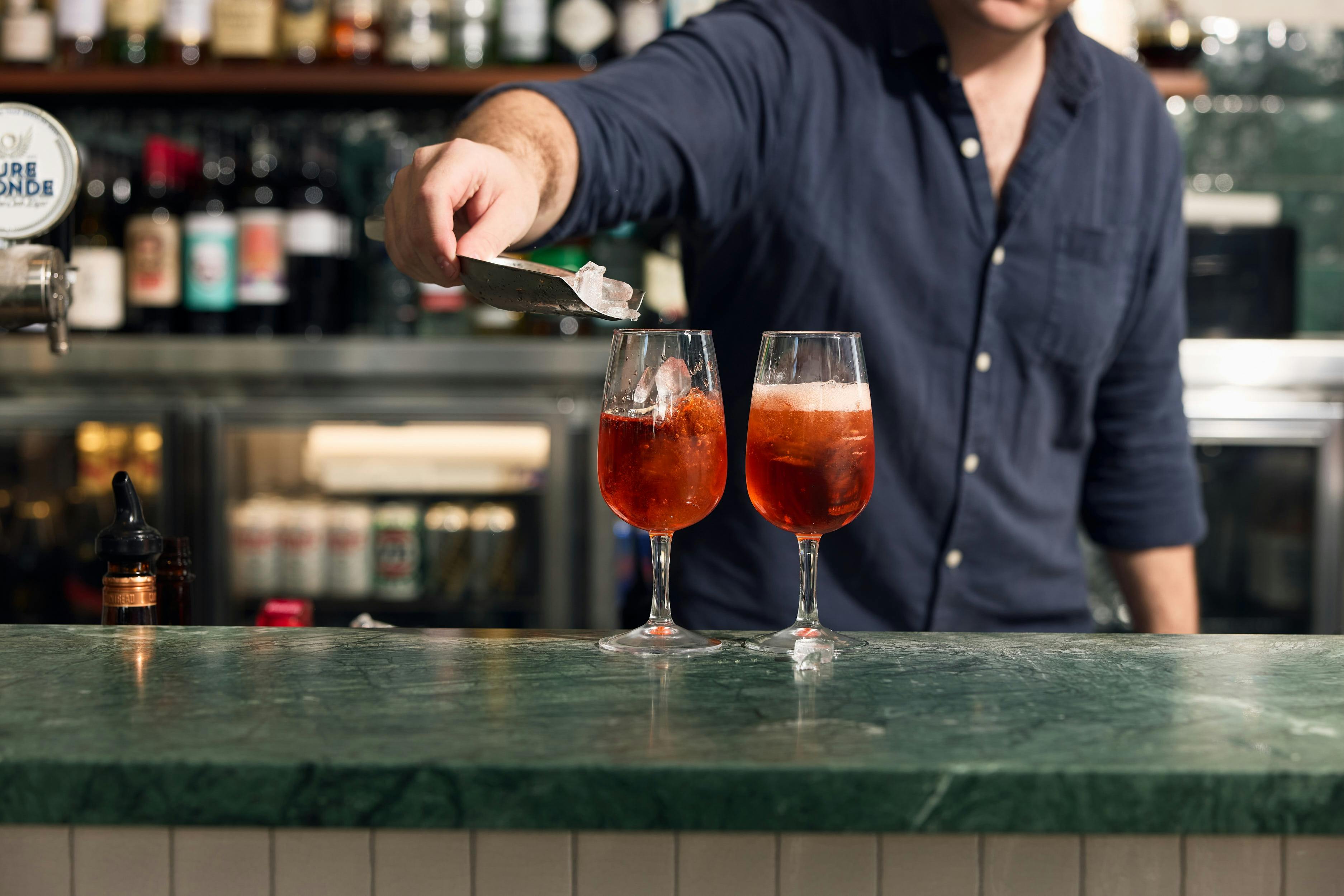 Two spritzes on a jade bartop, one being garnished with an orange slice