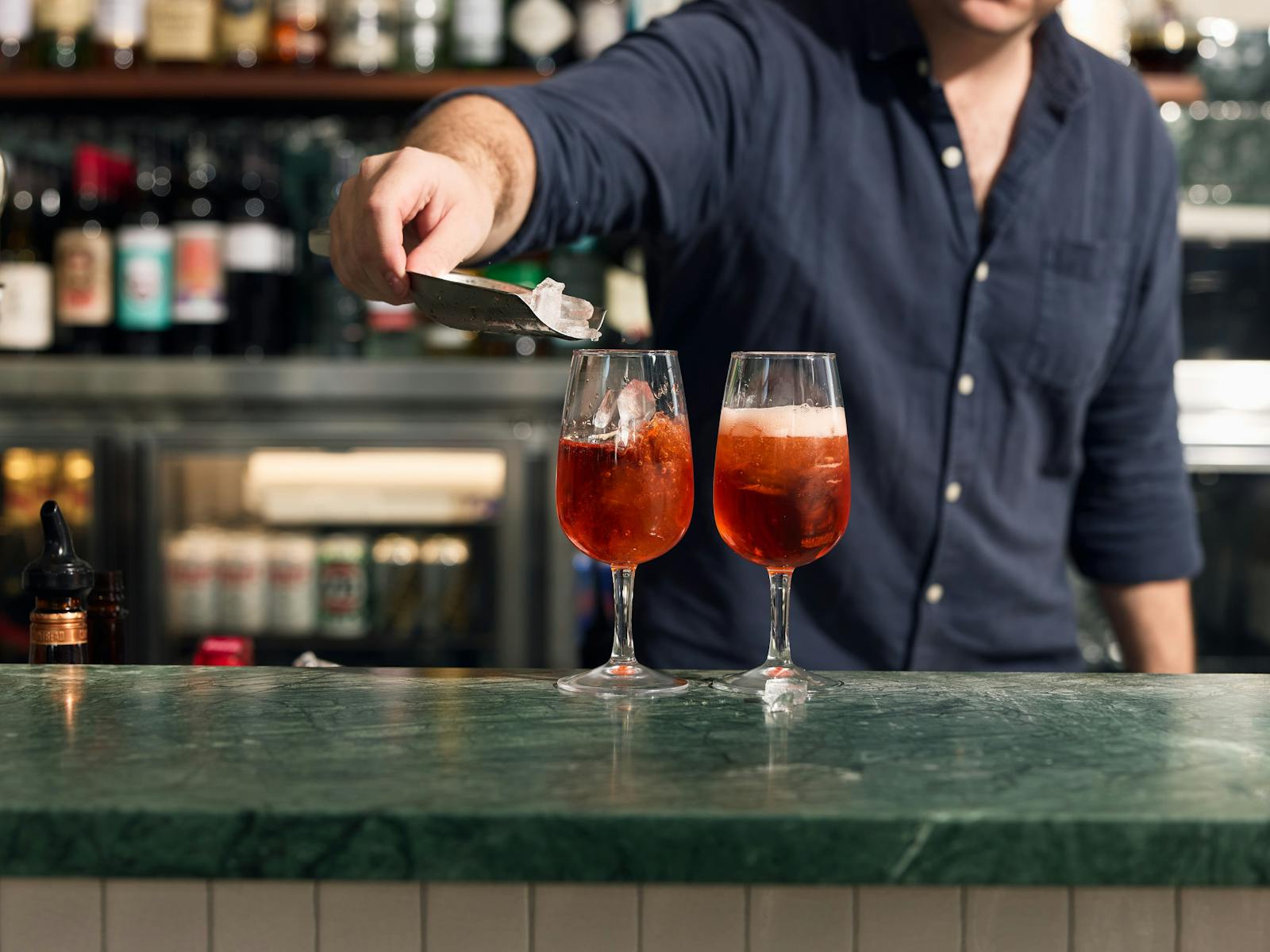 Two spritzes on a jade bartop, one being garnished with an orange slice