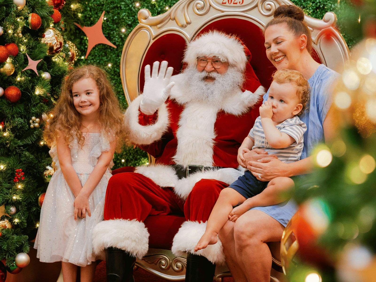 Mother with a baby and young child having their photo taken with Santa Claus