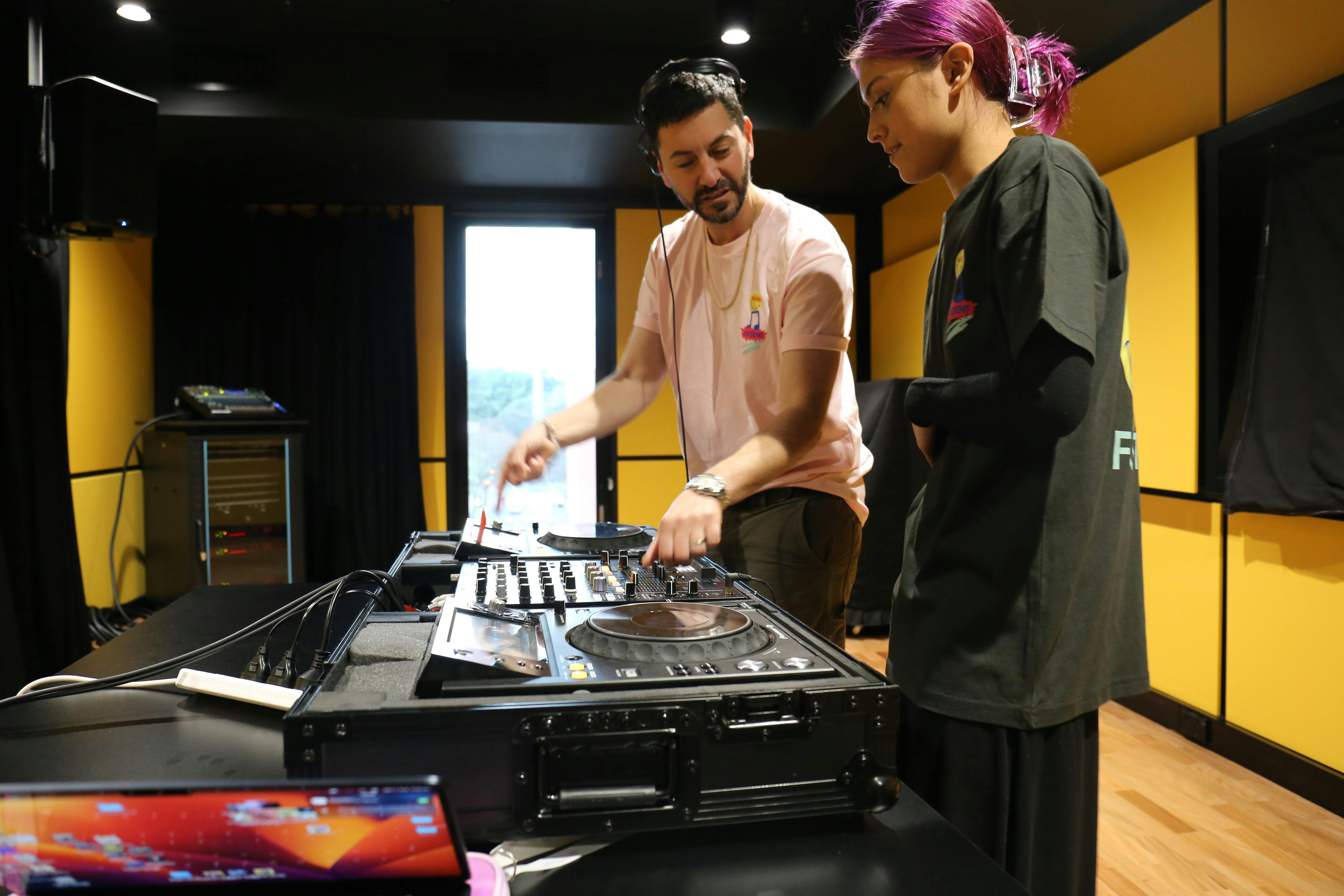 A photograph of two people looking at some DJ decks