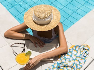 Woman with a sunhat, drinking a cocktail by the pool