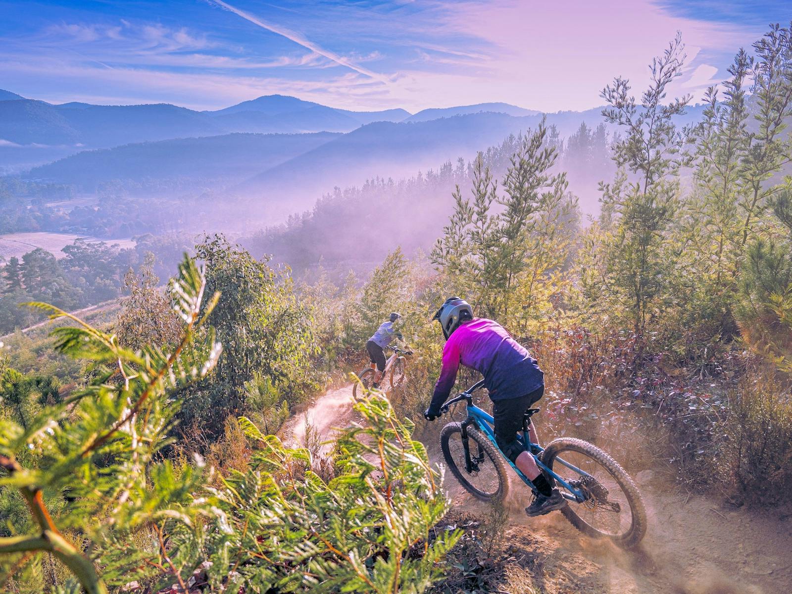 Two riders head down a mountain on their mountain bikes under a blue sky.